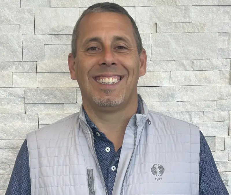 A man in a vest smiling for the camera.